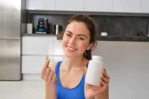 Happy young fit girl doing sports at home shows dietary supplements taking